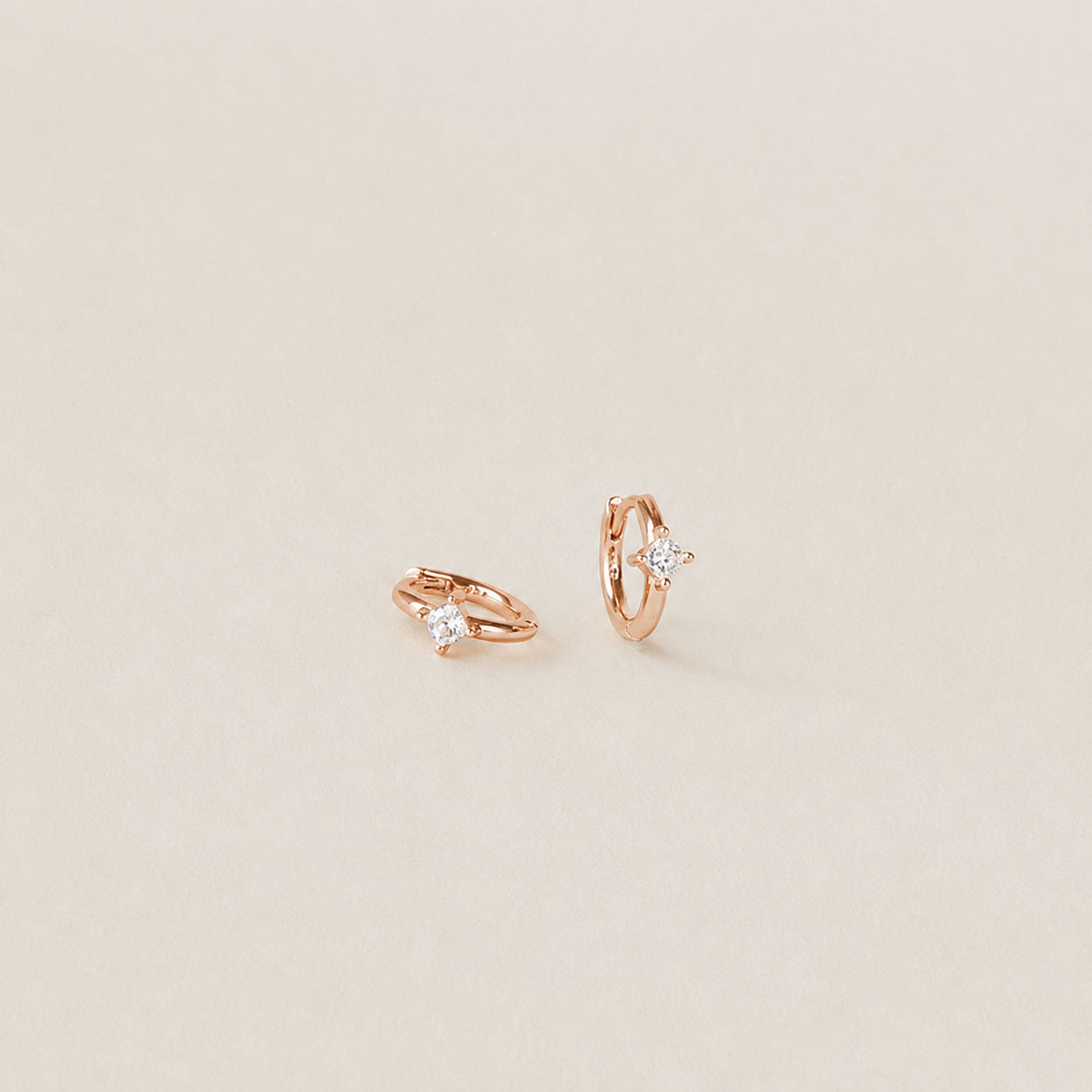 Pair of rose gold hoop earrings with small diamonds on a beige background